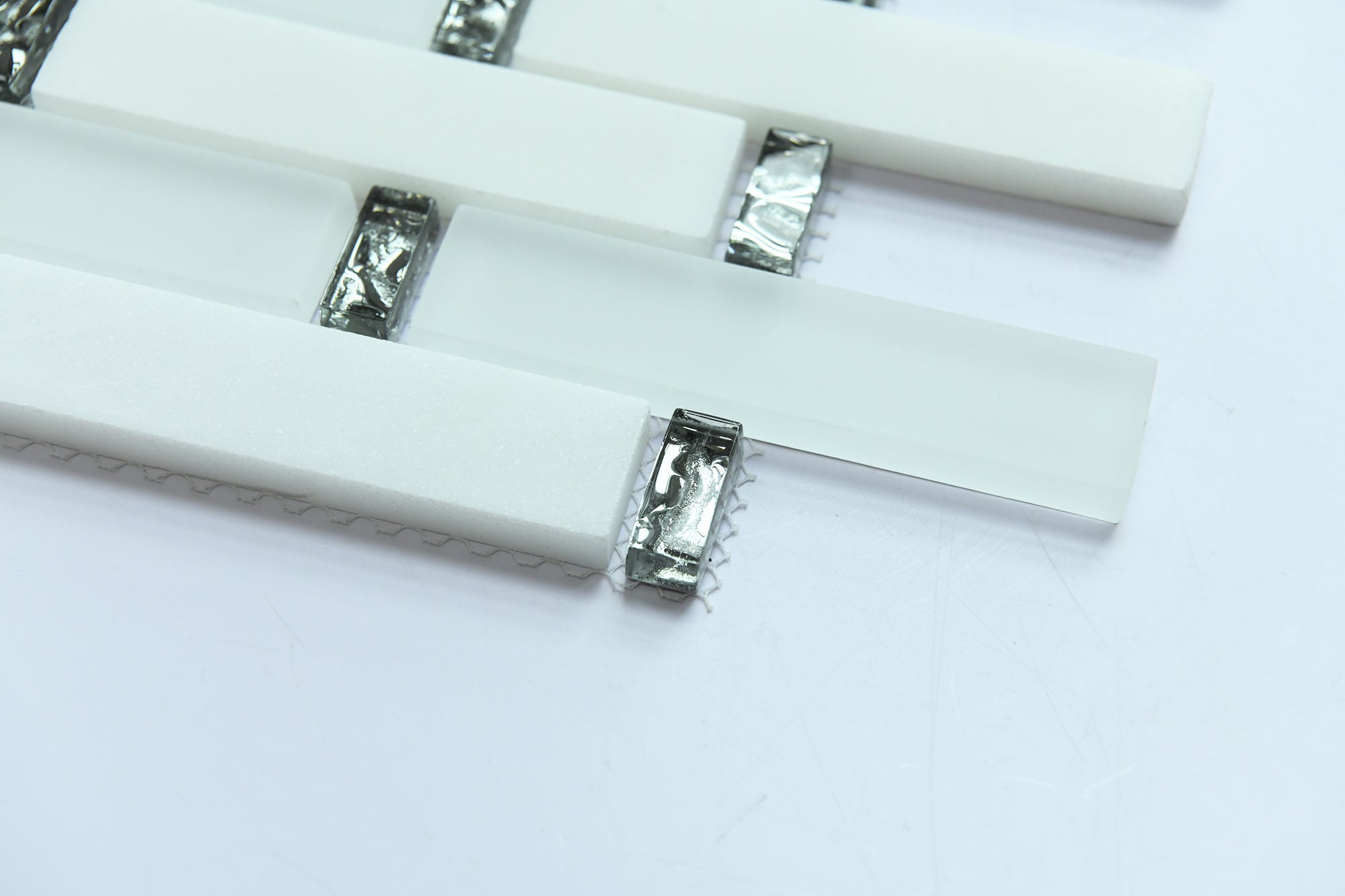 Close-up of white rectangular tiles with metallic clips on a light gray background